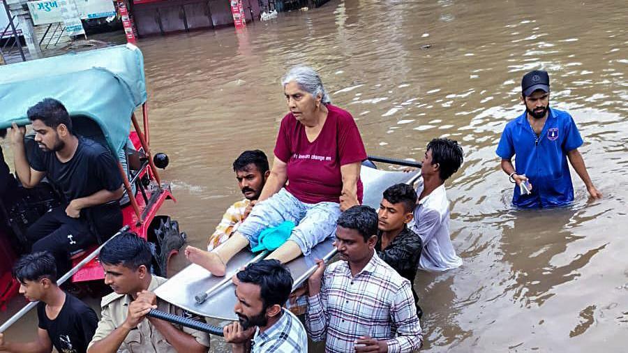 An elderly woman on a stretcher being carried over the shoulders of rescue officials in waist-high floodwaters in Vadodara city