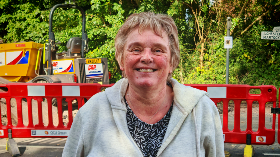 Image shows Yeovil resident Tina smiling at the camera, wearing a grey hoodie. Behind her roadworks are visible. 