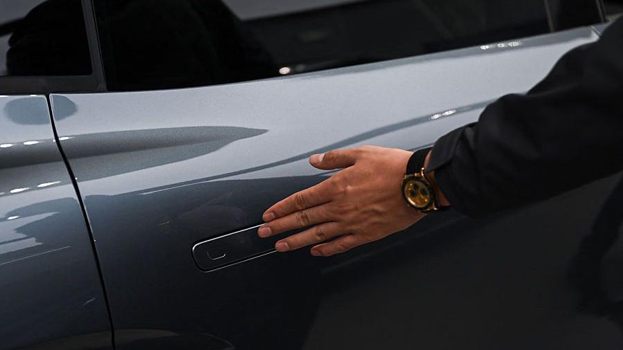 A man inspects an electric car, brushing his hand over its retractable door handle, during a vehicle roadshow in China.