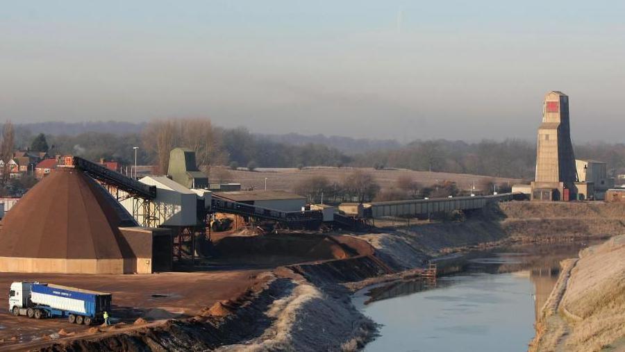 A large lorry can be seen at the mine, along with various storage buildings which are located next to a canal.