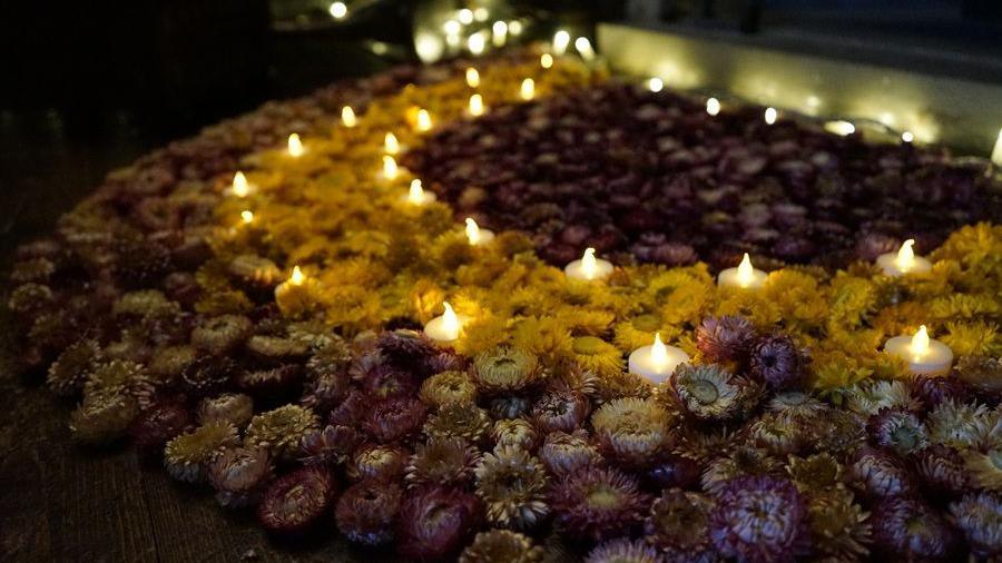 Flowers of many colours arranged in a pattern on the floor, with little candles dotted amongst them.