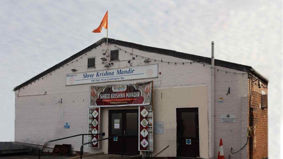 A white building with a black roof and red and orange flying from the top.
