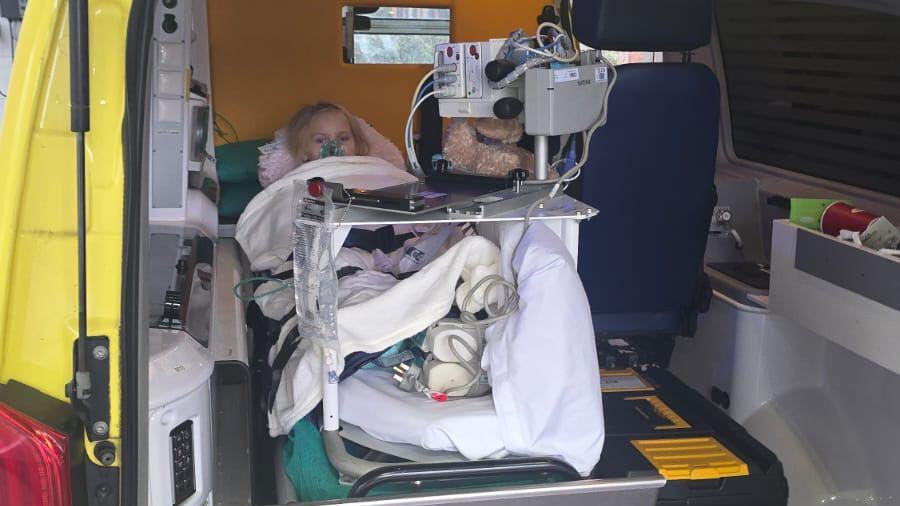 Lucy lies in an ambulance. She is covered in blankets and there is medical equipment around her.