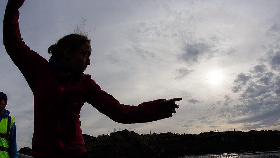 A sillouette of a woman throwing an object towards a body of water at night time