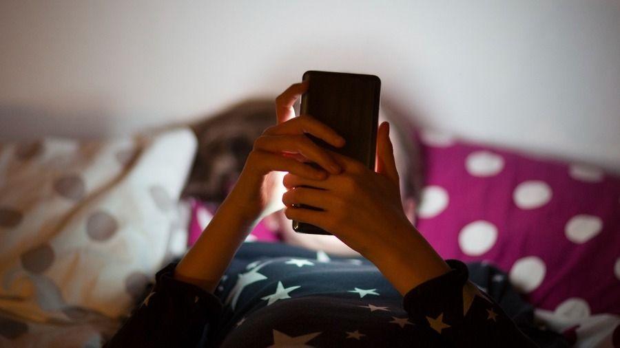 Child looking at phone on bed. 