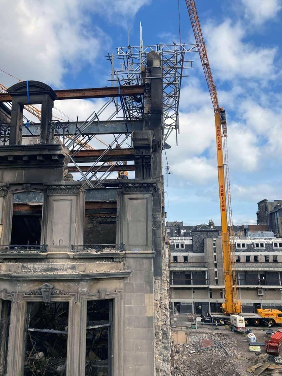 A fire damaged old building with parts of the wall supported by scaffolding and a large yellow crane at one side