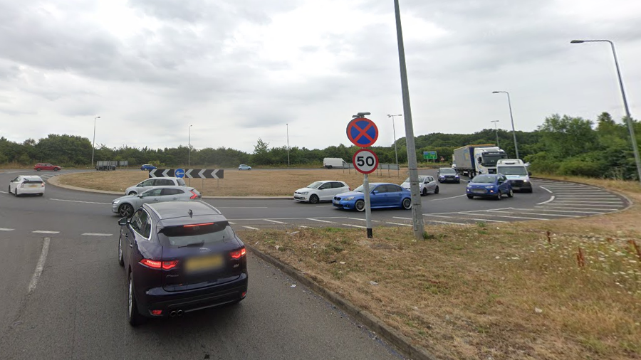 A two-lane approach to a roundabout. There are cars on the roundabout and a 50mph road sign.