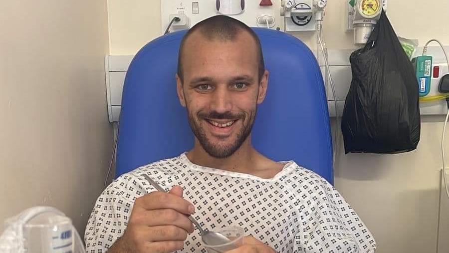 Dave Jones holding a spoon and plastic food pot and sitting on a blue hospital chair