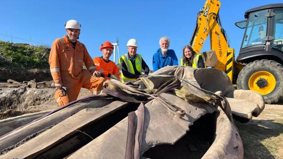 A group of men and women in high-visibility clothing surrounded around whale bones.