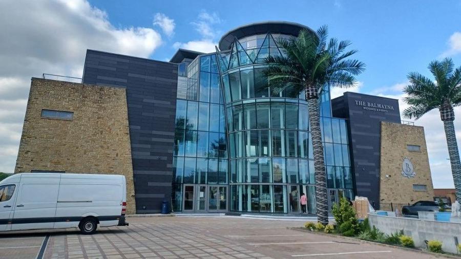 Exterior of Balmayna, which has a four-floor glass front topped by a crown and palm trees in the car park outside