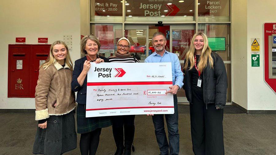 Staff from Jersey Post holding a large cheque for the charity. Four women and one man are holding the cheque. They are standing outside of Jersey Post's entrance. 