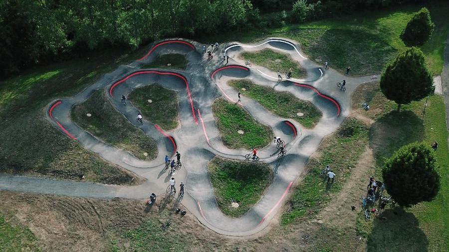 An aerial view of Chopwell pump track. Riders can be seen enjoying the track. Most of the course consists of a red track, which is marked with red lines running around its high corners. A smaller white track for beginners is located at the top of the facility.