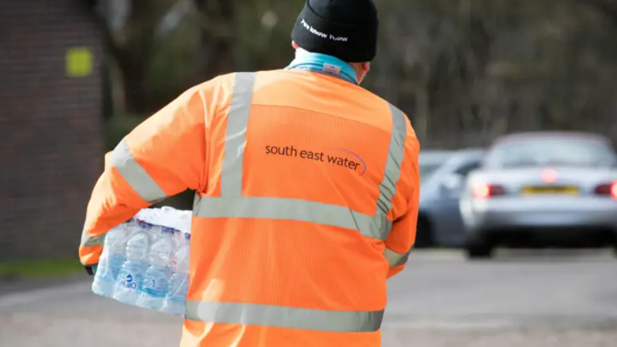 A South East Water worker pictured carrying a package containing several bottles of water following a water outage. He is wearing an orange high-viz jacket.