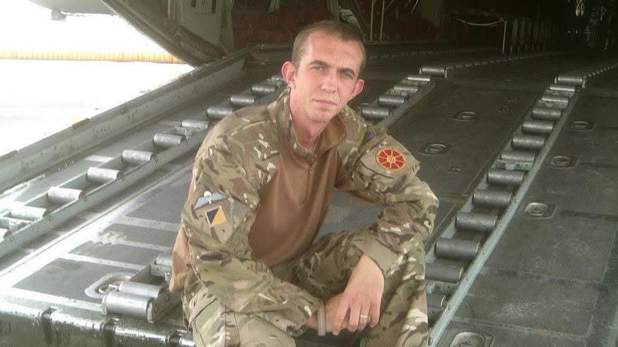 Cameron Alexander in his Army uniform sitting on a large metal door of an aircraft.