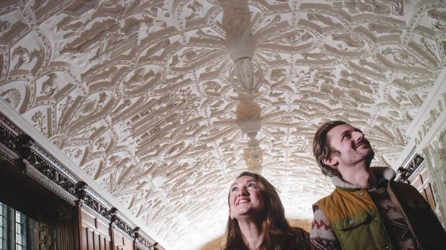 Two people looking up at the ceiling which has different moulds with different depictions.