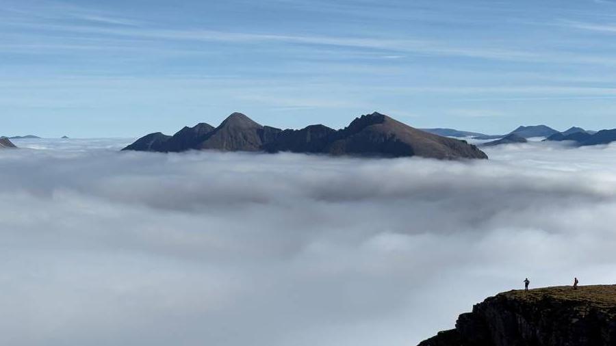 Jagged mountain tops rise above a thick blanket of clouds under a clear blue sky.