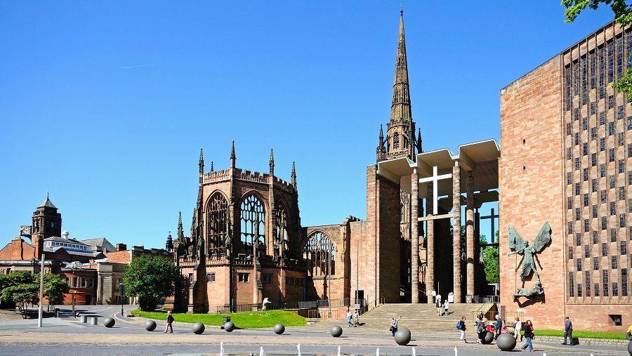 The old Coventry Cathedral, a partially demolished 14th Century building made from red sandstone, next to the new building made from light brick and glass.