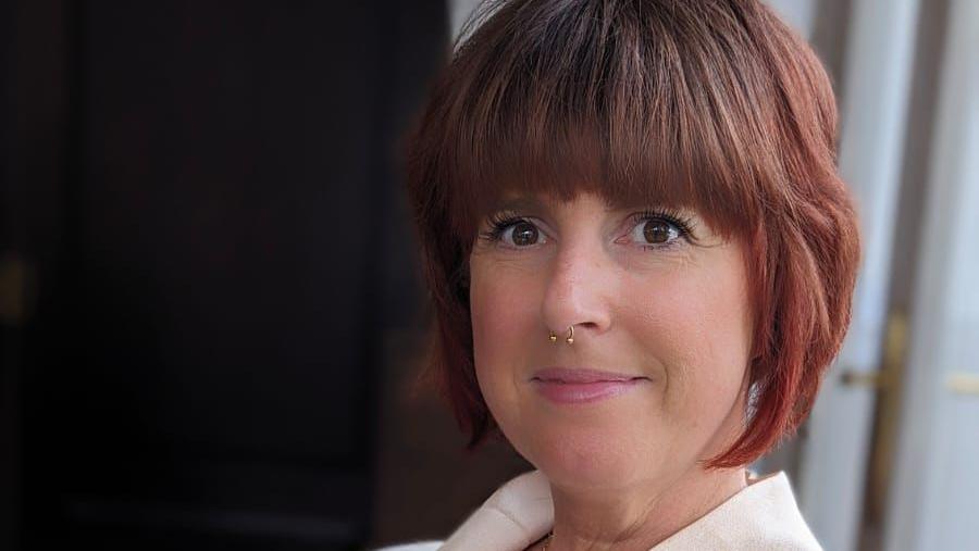 Catherine Warrilow smiles at the camera. She has red hair, nose jewellery and wears a white top.