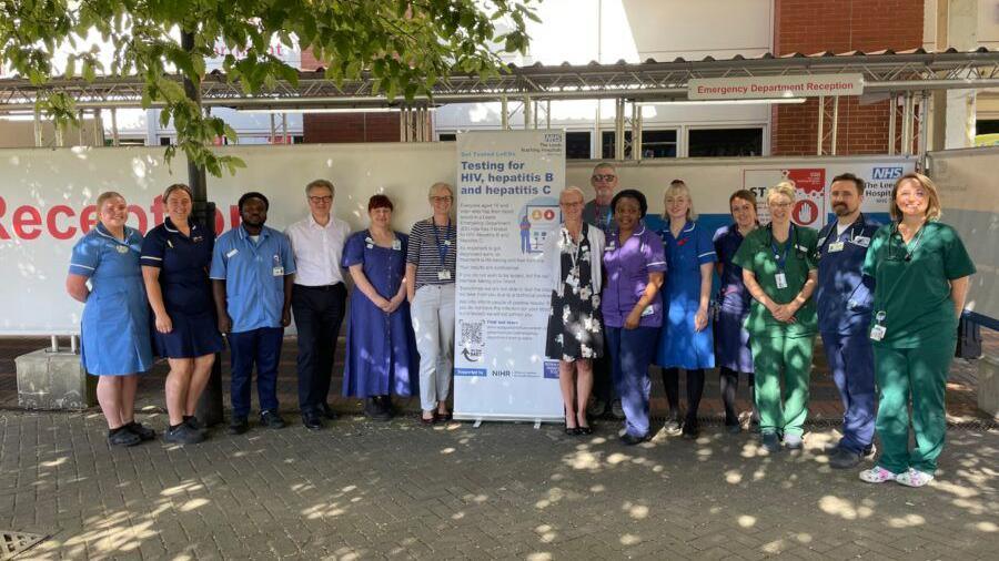 NHS staff standing next to sign about testing for HIV, hepatitis B and hepatitis C