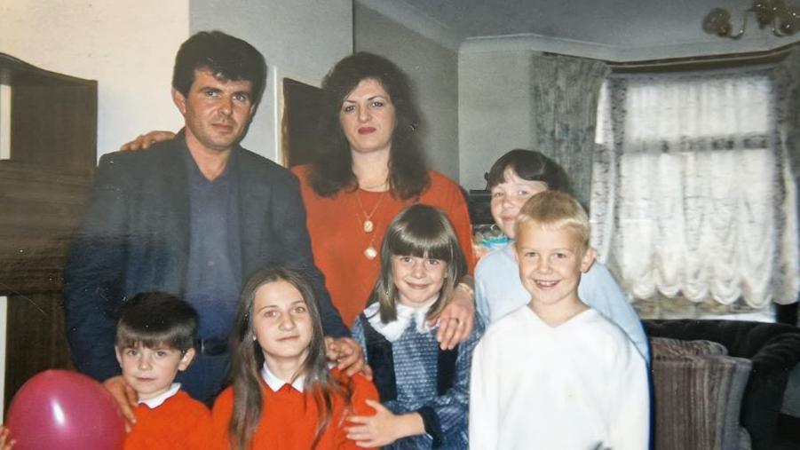 An old family photo of the Durakus, with two children in school uniforms and others in plain clothes. The parents have their arms around them. 