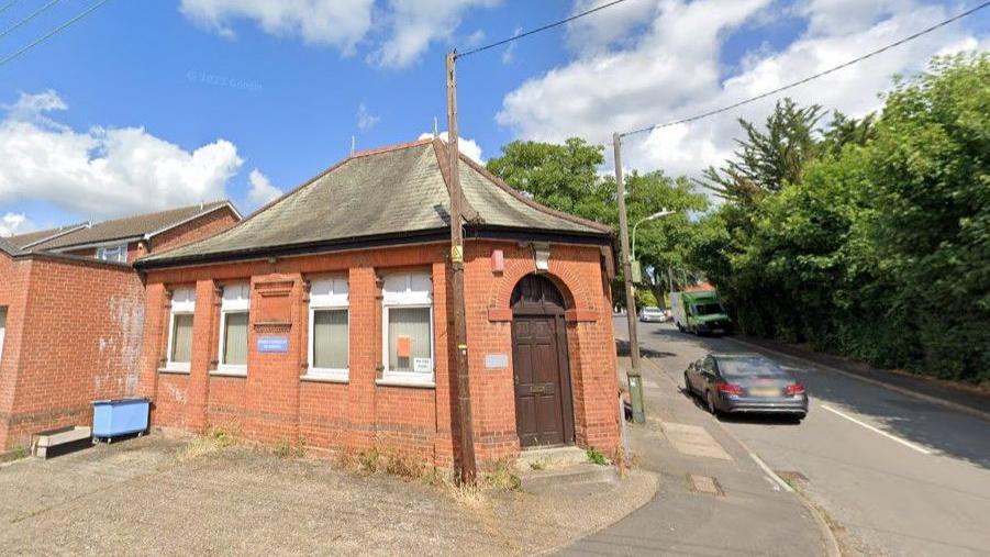 A red brick one storey building on a street corner. 