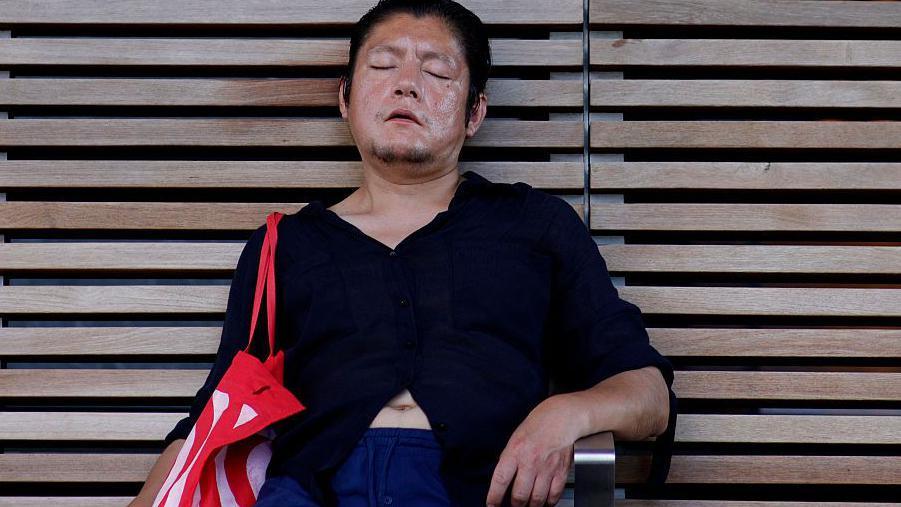 A man rests in the shade on a bench in Midtown Manhattan during a heatwave in New York City on 3 July