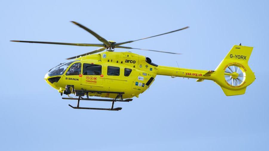 Yorkshire Air Ambulance, a yellow helicopter, in a blue sky.