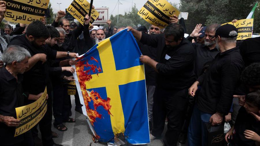 Iranian worshippers burn a Sweden flag during a protest against Koran burning in the Swedish capital Stockholm, at the Imam Khomeini Grand Mosque after Tehran's Friday prayer ceremony, July 21, 2023