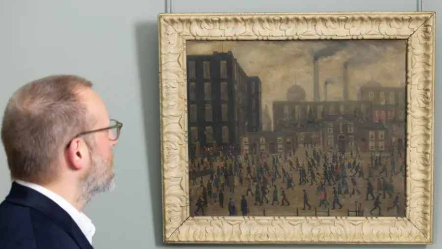 A man looks at Lowry's Going To The Mill as it hangs in a frame on a wall. It depicts an industrial Manchester landscape with matchstick figures walking in the foreground.