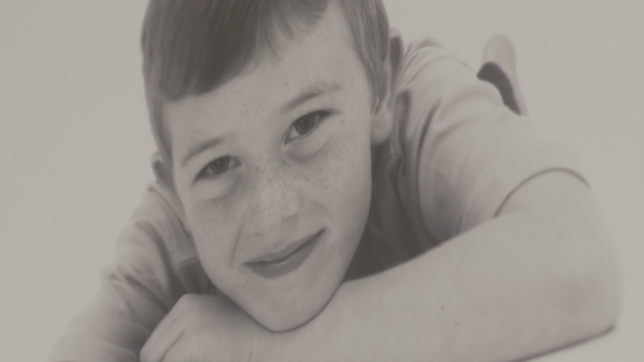 A formal black and white photo of Andrew when he was much younger. He is lying down with his chin on his hands. 