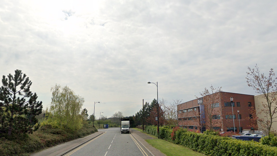 The Tuscany Way area of Altofts. Pictured is a relatively narrow road, with office-like buildings on one side, behind some hedges, and some trees on the other