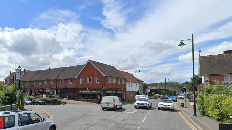 A Google StreetView of a busy intersection. There are lots of cars and red buildings line the roads