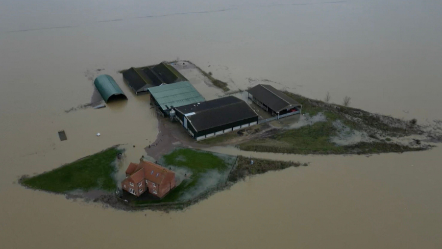 A farmhouse, completely surrounded by water.  Some of the farm buildings stand on dry land, but the fields are completely submerged.