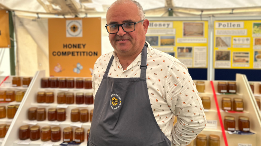 Adrian Doyle smiling at the camera in his apron is wearing black framed glasses