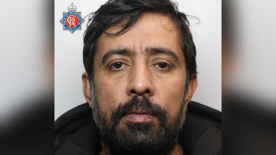 Mugshot of Daniel Hashmi. He has dark hair and a beard, and wears a dark coat.