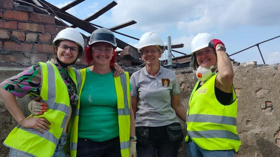 Four female conservations wearing high vis jackets and hard hats smile and pose for a photograph at the building site.