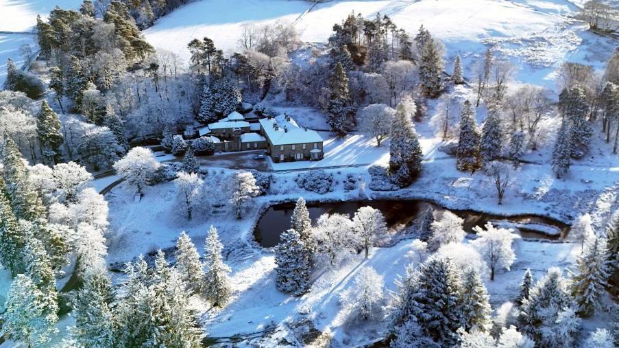 Aerial photograph of a property in Northumberland, showing a snowy scene. Fields and trees can be seen covered in snow across the landscape, with a large house in the middle of the image. 