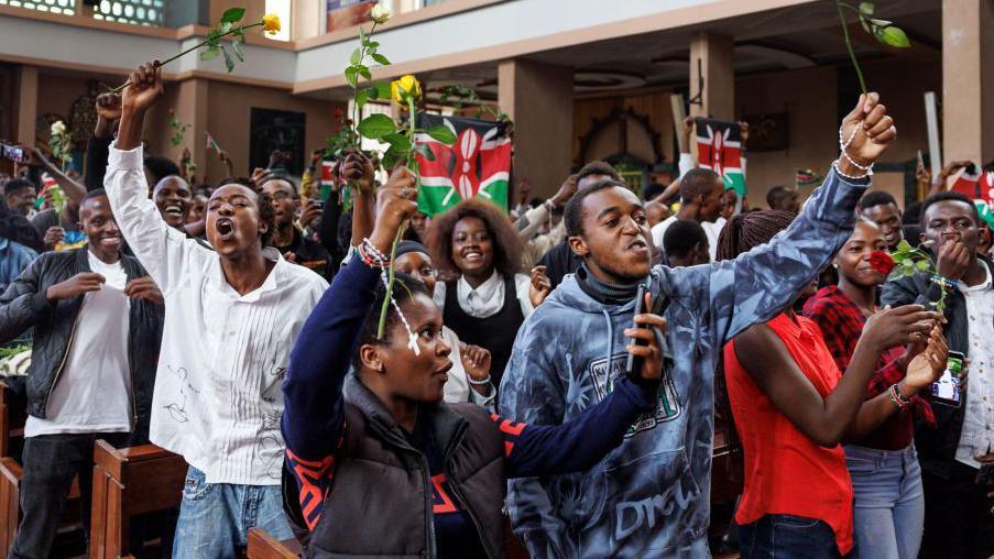 Young people holding up roses sing during a special service at the Holy Family Basilica in Nairobi to honour those who lost their lives in anti-tax protests - July 2024