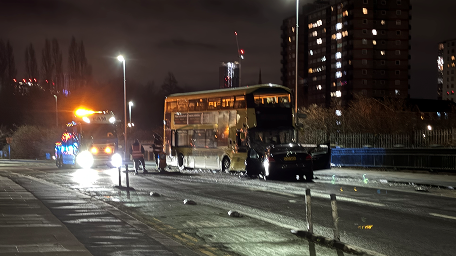 A damaged yellow bus and a black car illuminated by street lights and a rescue vehicle