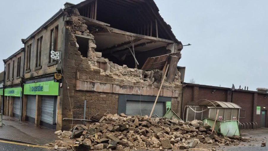 Side view of a Co-op with the brick wall partially collapsed