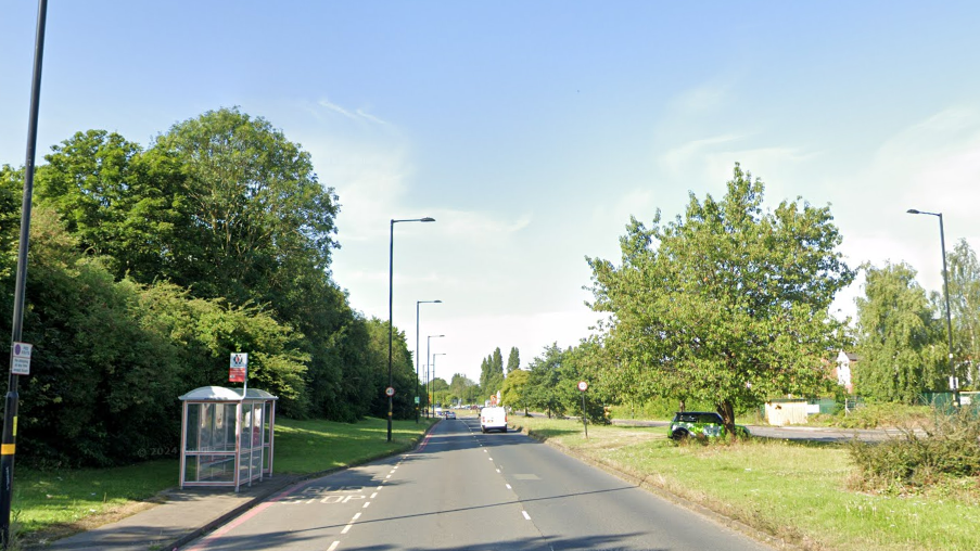 The Kingfisher Road in Birmingham lined by green trees and grass with a bus stop to the left side