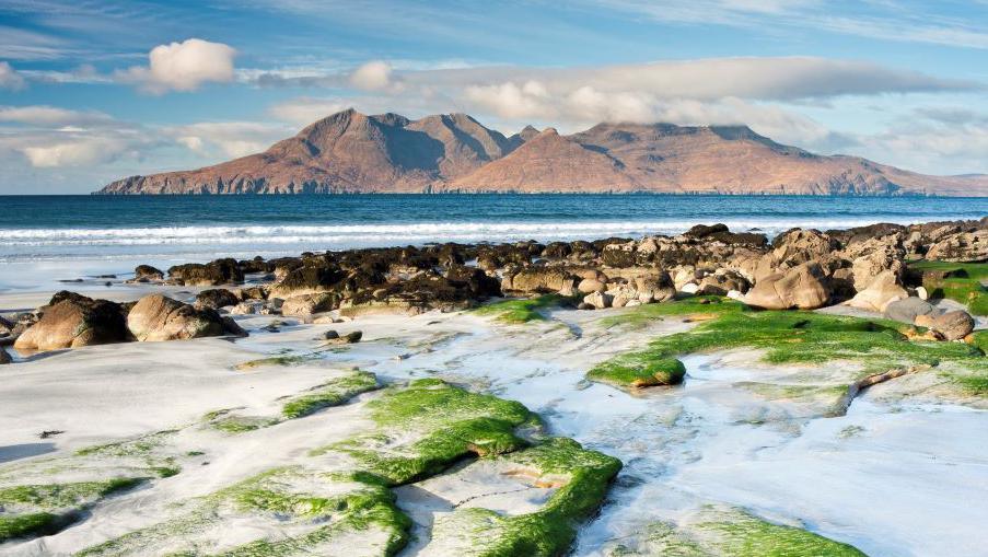 The Isle of Rum in sunshine and pictured from a rocky beach