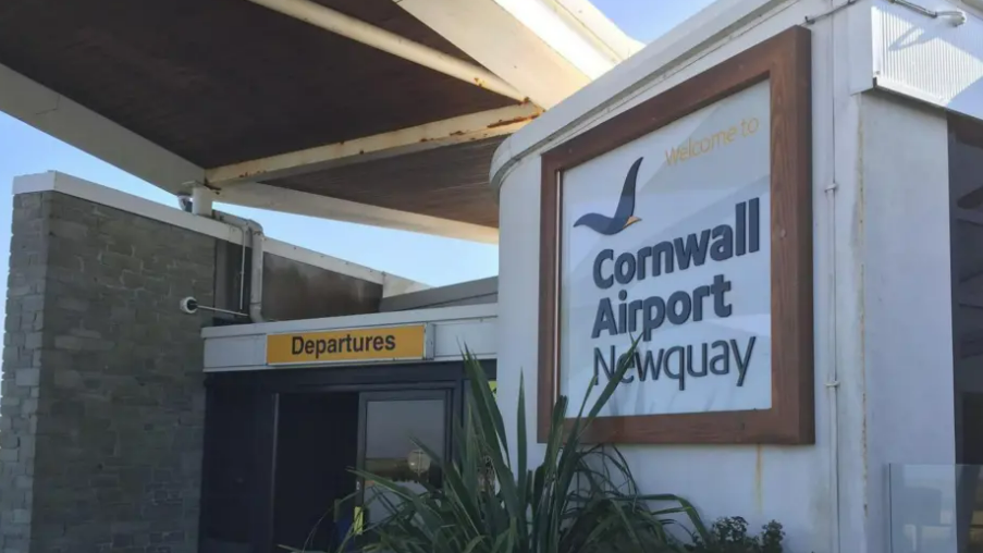 Cornwall Airport Newquay's entrance with sign reading the name of the airport and a yellow rectangle sign reading departures.
