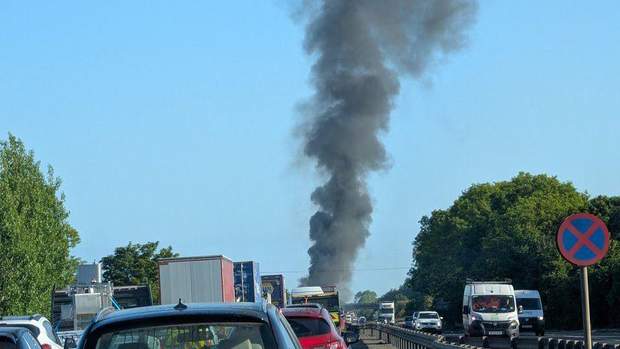 Queues of traffic towards the scene of the fire with a thick plume of black smoke rising into the sky