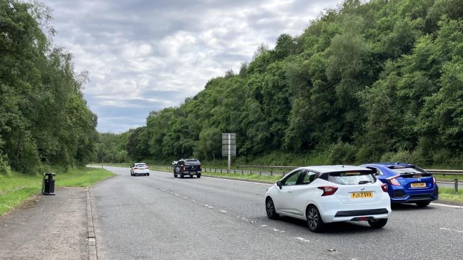 several cars driving on a road under a cloudy sky