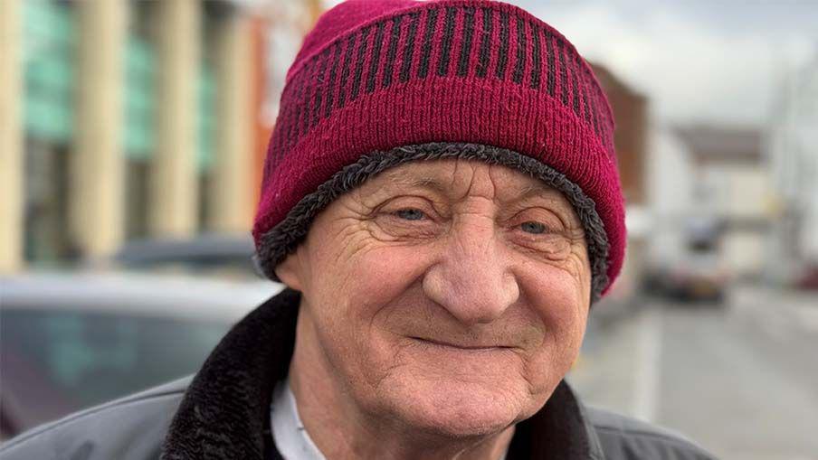 Head shot of Nigel Mountain, he is smiling and is wearing a dark red woolly hat