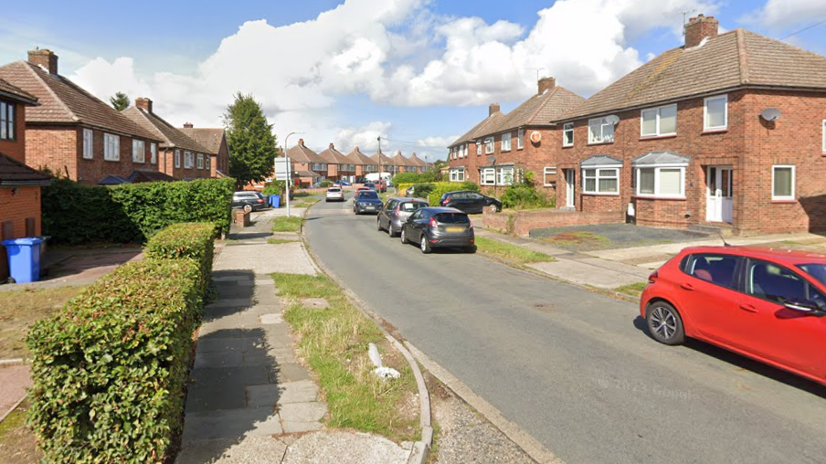 Street view image of Chesterfield Drive on a sunny day in 2023. It is a residential area with houses either side of the road and cars parked next to the pavement on the right hand side. 