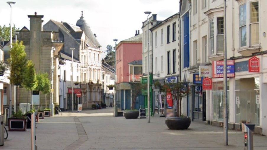 A section of George Street in Pontypool shows shops including Greggs on the right hand side, with street furniture including large plant displays.