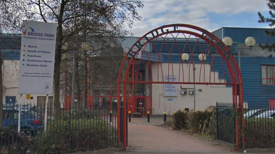 Exterior view of Bridge Park Community Leisure Centre in showing its entrance archway, fencing, and signage.