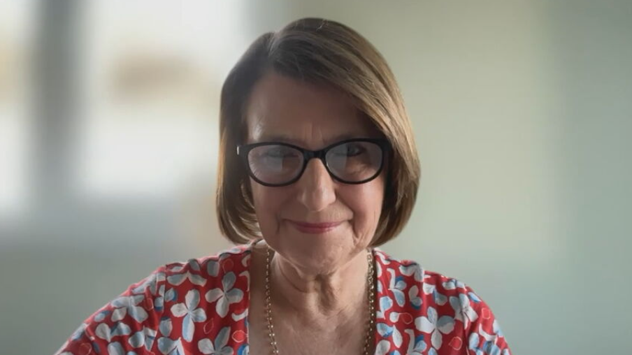Patient Safety Commissioner Karen Titchener sits indoors facing the camera, wearing dark-framed glasses and a red patterned top, with a softly blurred background.